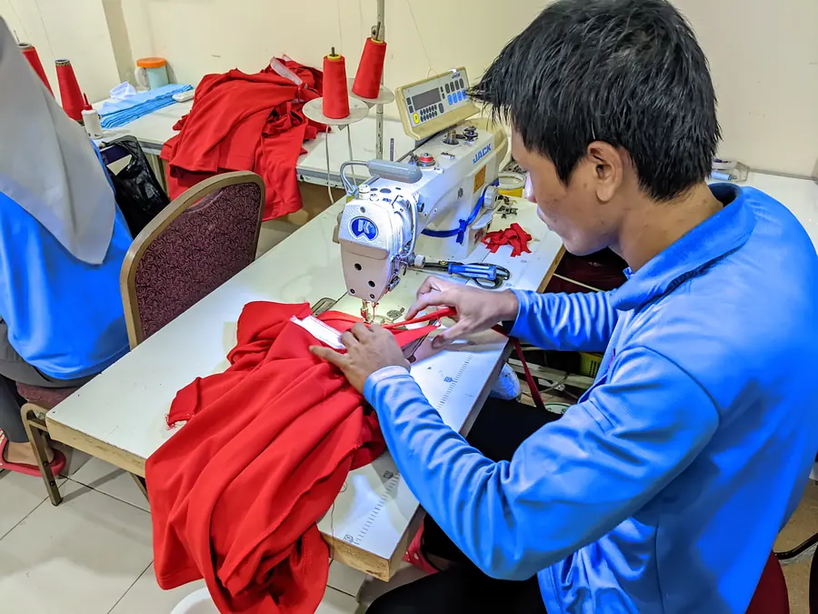 Penjahit mengerjakan kain merah di mesin jahit
